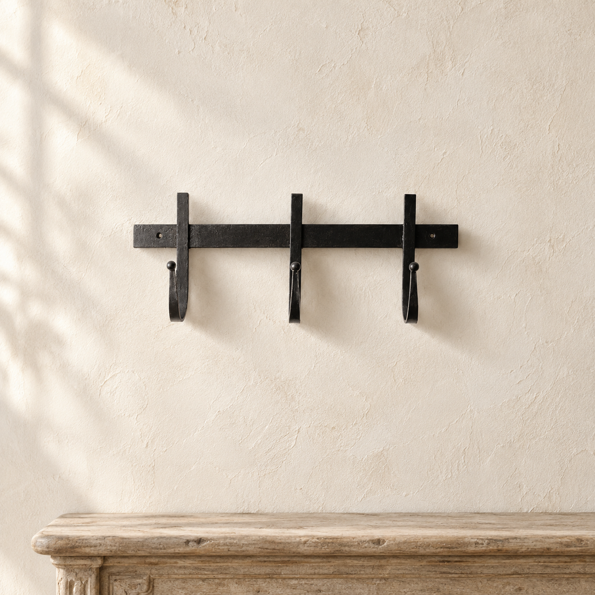 Black chunky iron three-hook wall rack on a French provincial wall